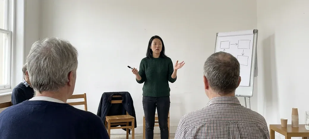 Maya Chen talking to a small group beside a flip chart in the workshop room