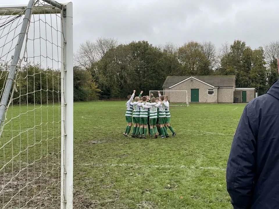 The under-10s celebrating at the far end of a muddy pitch