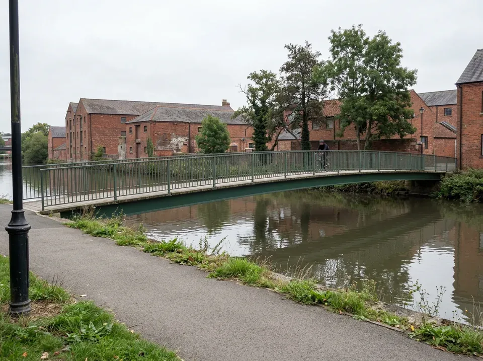 A slim green steel footbridge with a timber deck over a narrow river