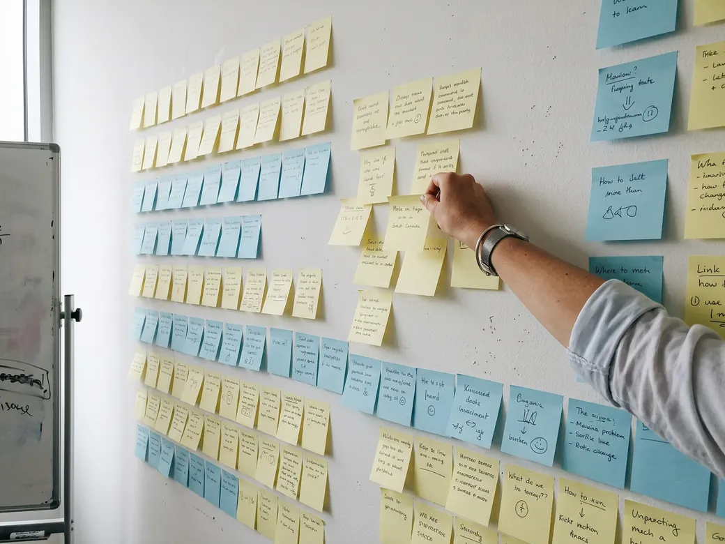 Hands sorting yellow and white sticky notes on a glass wall in an office